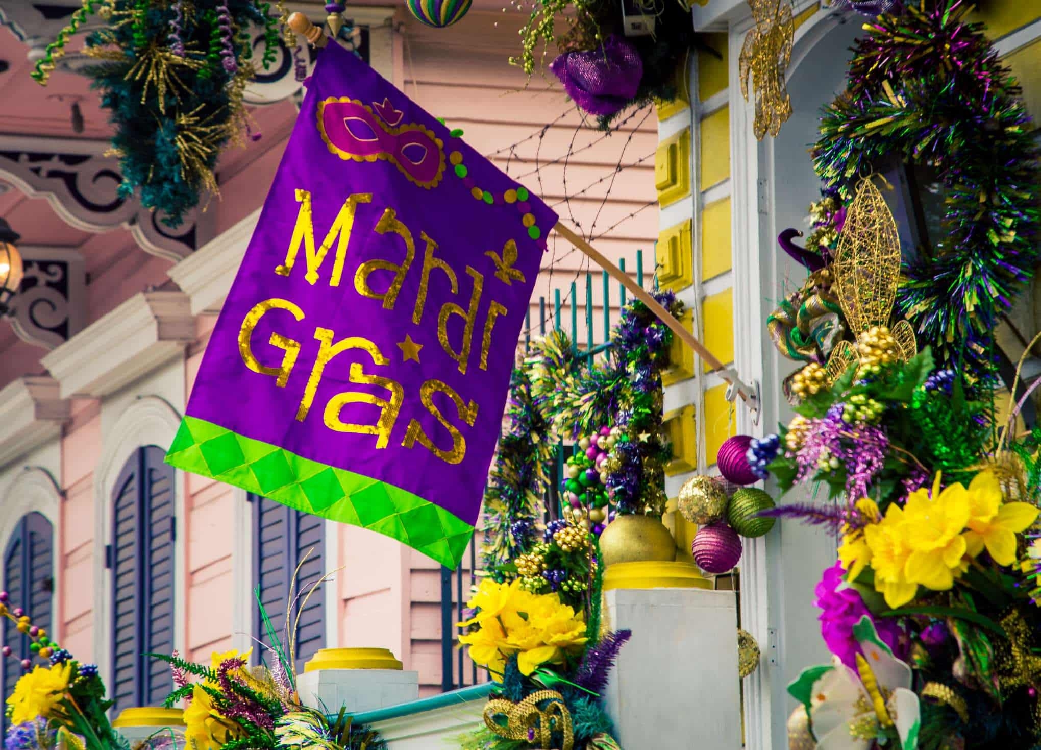 A Mardi Gras flag and decorations adorn a wrought iron fence in New Orleans