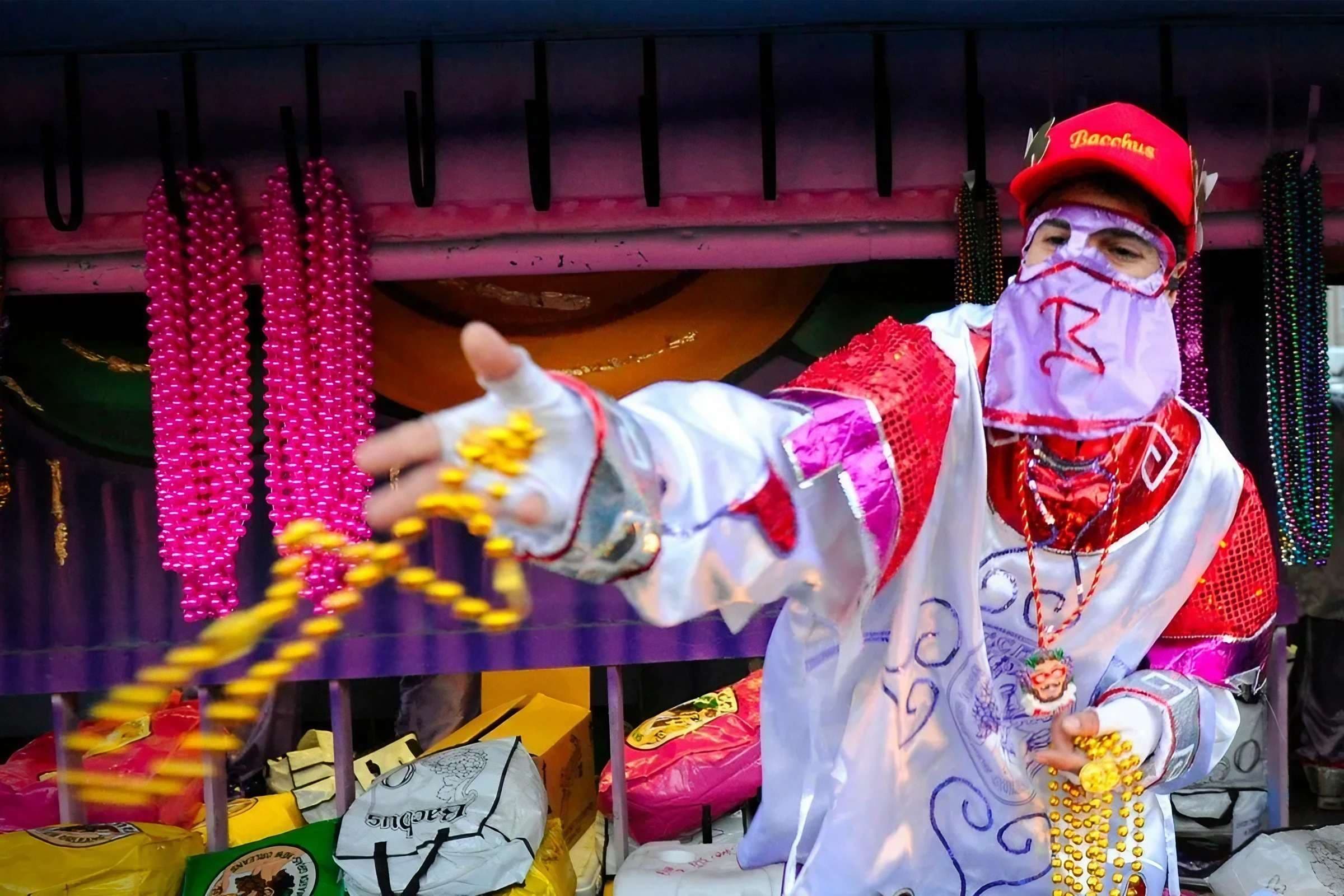 A member of the Krewe of Bacchus throws a strand of yellow Mardi Gras Beads into the crowd below