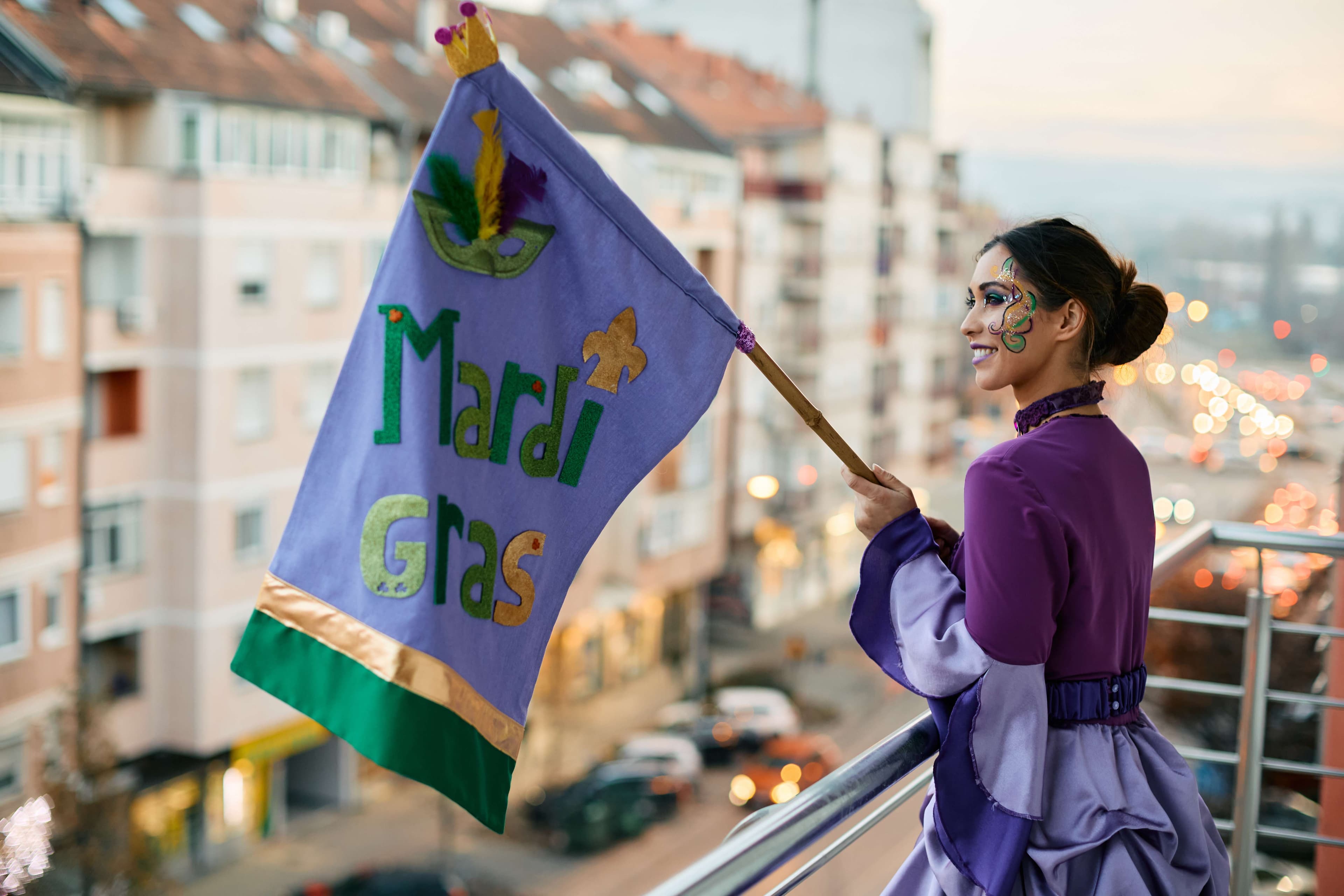 Mardi Gras 2023 attendee waving a Mardi Gras flag from a balcony in New Orleans